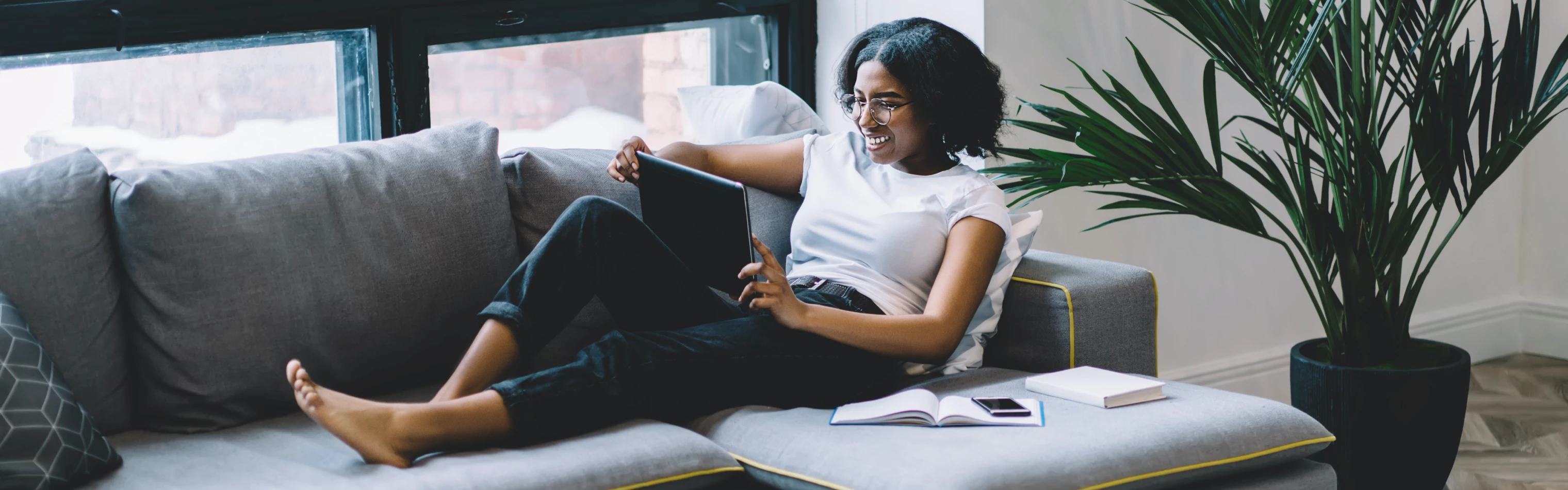 Black woman holding tablet device and lounging on couch.